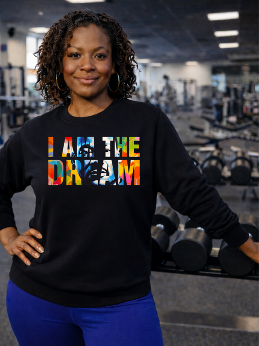 A Black woman wearing a black sweatshirt with 'I AM THE DREAM' text in colorful letters in a gym setting.