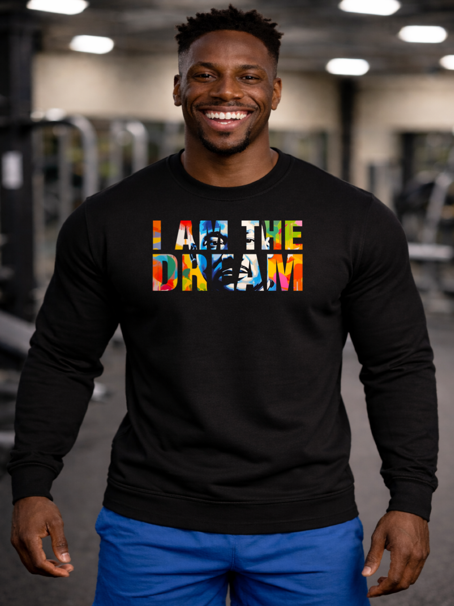 Black man standing in the gym wearing a black sweatshirt with colorful text that says I am The Dream
