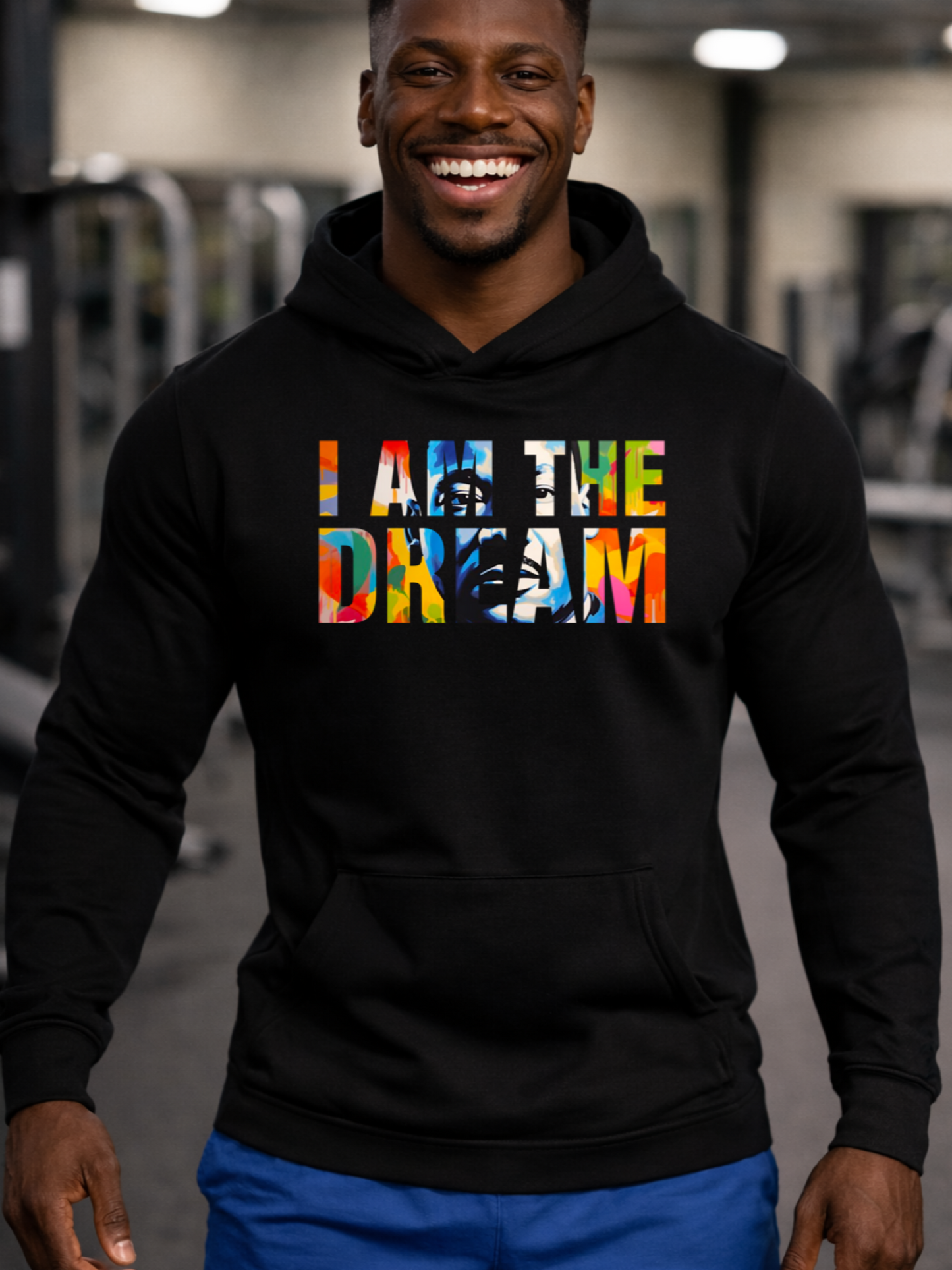 A Black man wearing a black hoodie with 'I AM THE DREAM' text in colorful letters in a gym setting.