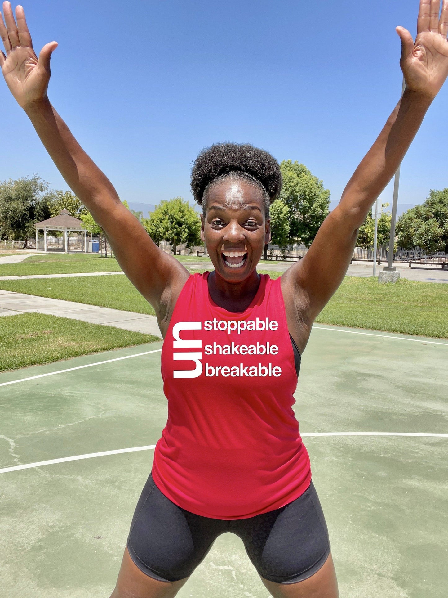 Black Girl jumping in Red workout muscle tank. The shirt says Unstoppable Unshakeable Unbreakable