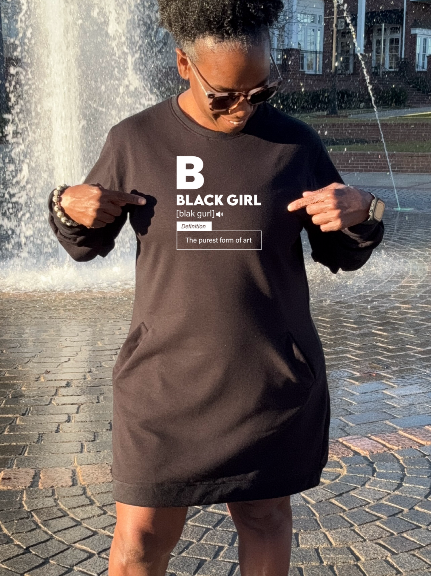 A Black woman wearing a black sweatshirt dress that says Black Girl the purest form of art