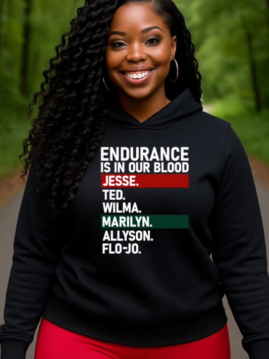 A black woman wearing a black hoodie with Endurance is in our Blood text in a forest setting