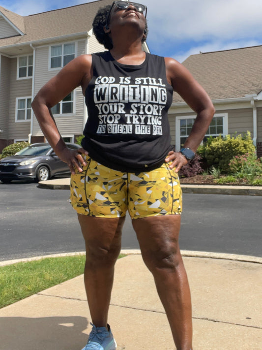 A runner wearing a black muscle tank top with a text graphic that reads 'God IS STILL WRITING YOUR STORY, 