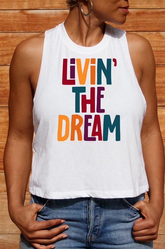 A young lady wearing a white racerback crop tank top with the text 'LIVIN' THE DREAM' printed in colorful letters, 