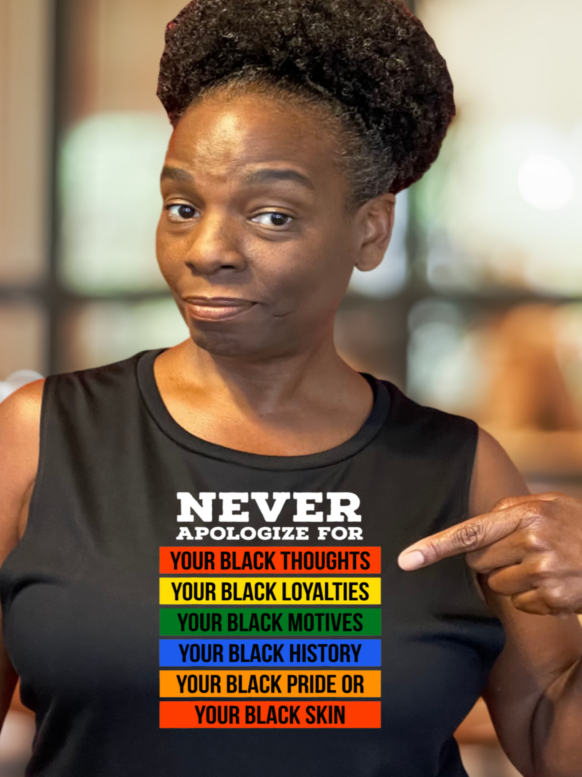 A woman wearing a black muscle tank top with Never apologize for your blackness on it, standing in a room with bookshelves.