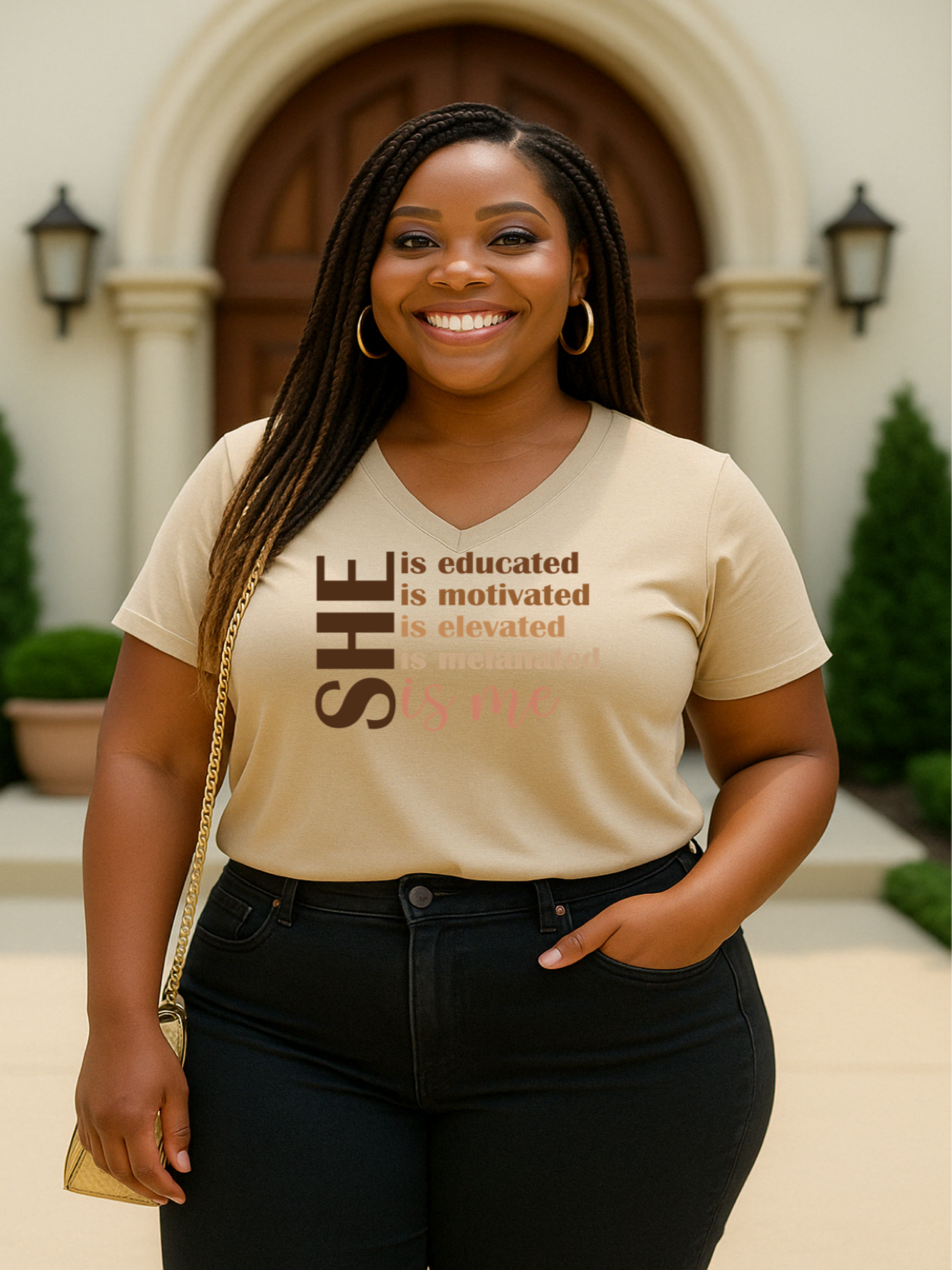 A woman smiling and wearing a black V-neck t-shirt with the text 'SHE is educated, motivated, elevated, powerful, and purpose-driven. And yes—SHE is ME.