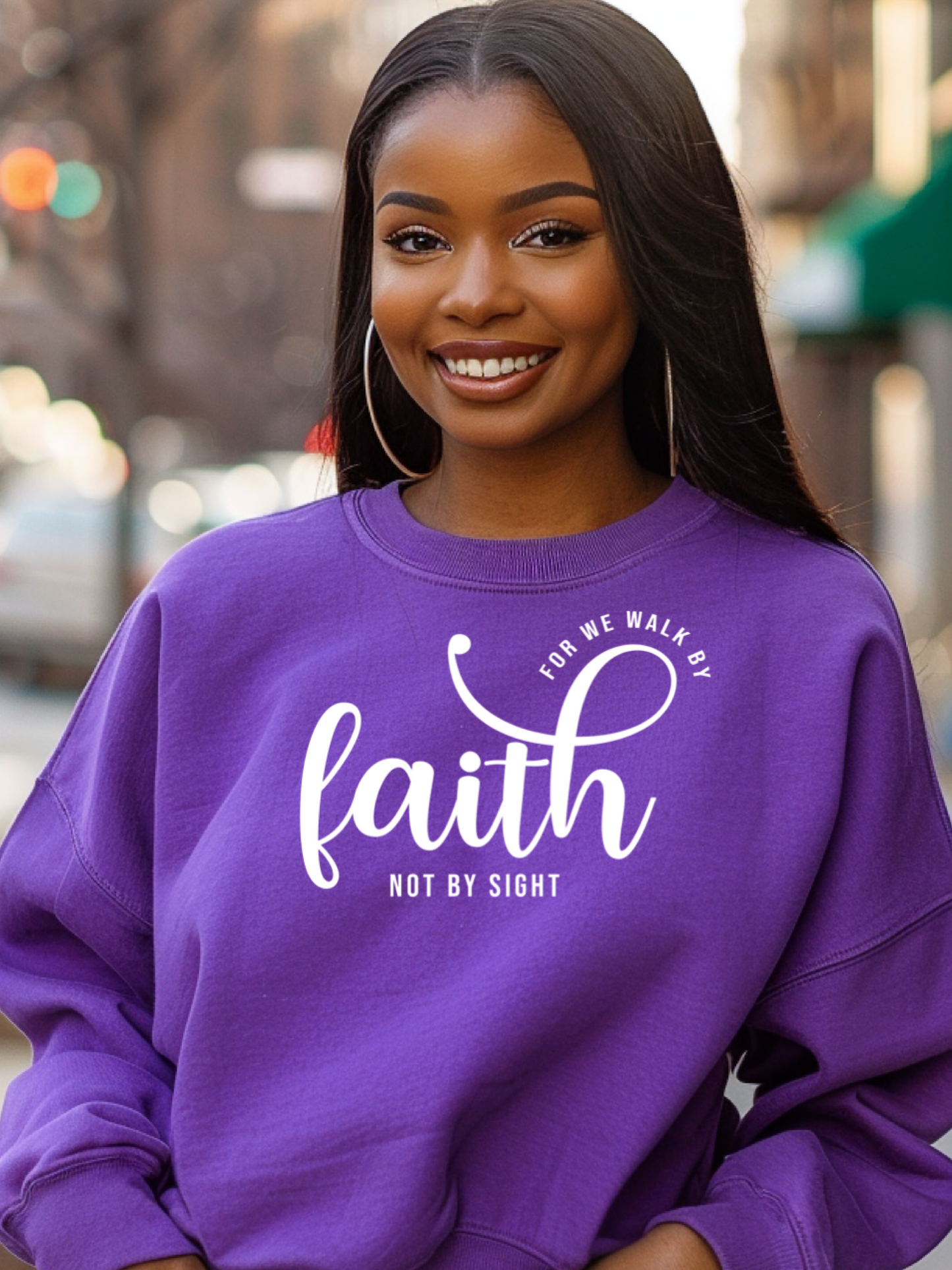 Woman wearing a purple sweatshirt with 'For we walk by faith not by sight' text.