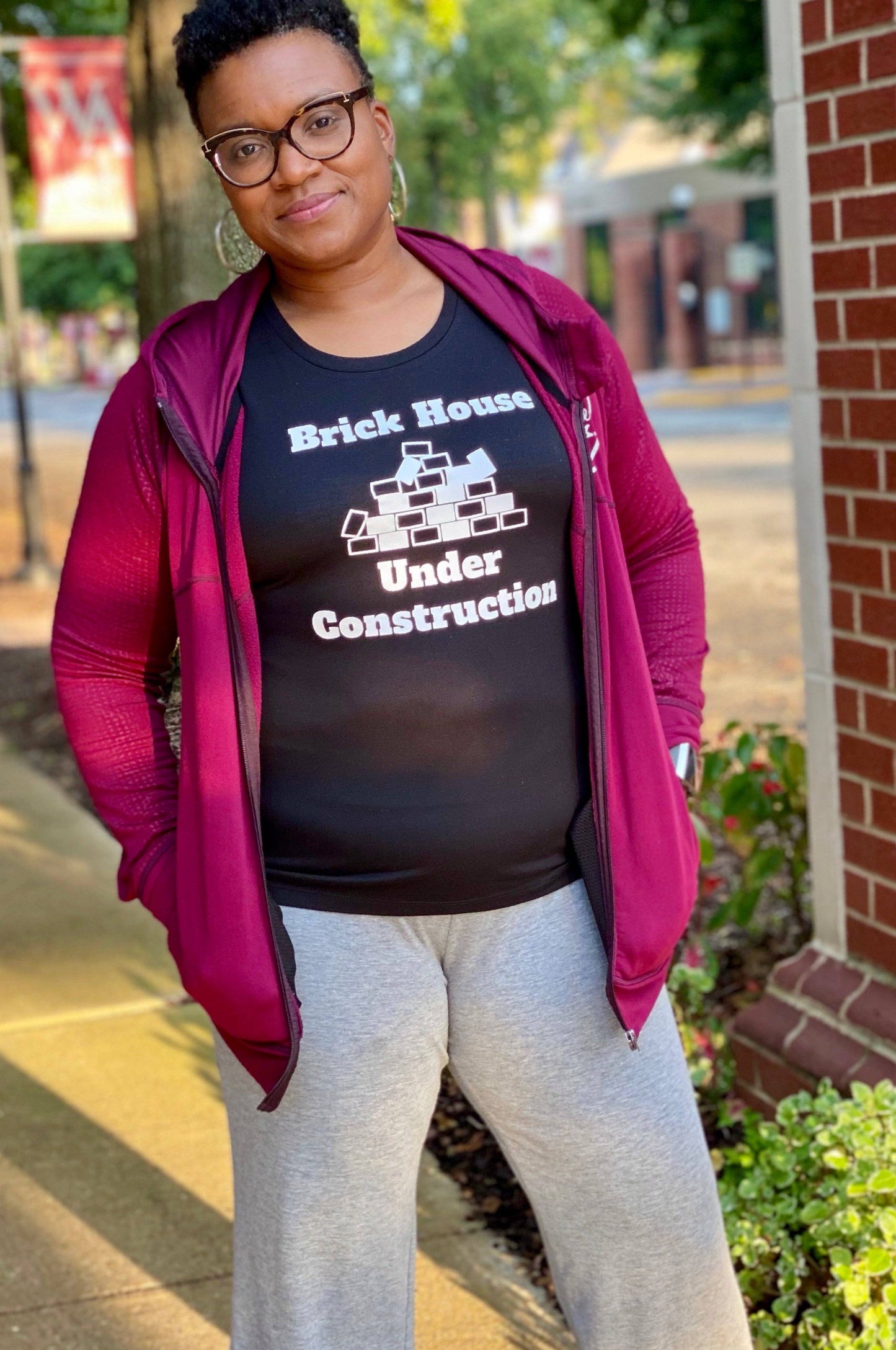 Black girl wearing glasses , gray sweats and a activewear tank top. the tank is black and says Brick house under construction. 