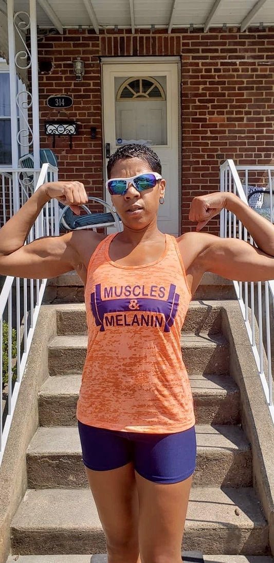 Black girl doing a double biceps pose wearing a orange muscles & melanin tank top